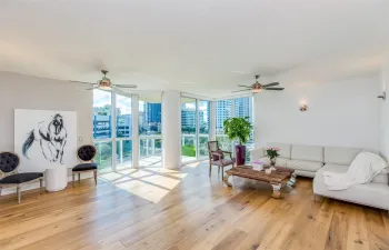 Living area featuring hard wood flooring, open balcony & floor to ceiling windows.