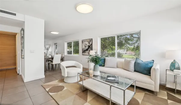 Bright and inviting, the living area is bathed in natural light from oversized windows that offer a serene view of the lush greenery outside. Clean lines, soft neutral tones, and stylish modern furnishings create a calm and comfortable space perfect for relaxing or entertaining.