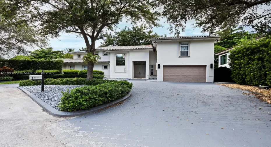 Beautiful two-story home with stucco exterior, tile roof, mature oak tree, professional landscaping with river rock accents, paver driveway, and attached two-car garage.