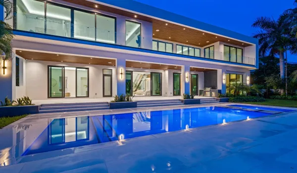 Stunning twilight view of the modern residence featuring glass-lined balconies, covered terraces, and a glowing pool centerpiece.