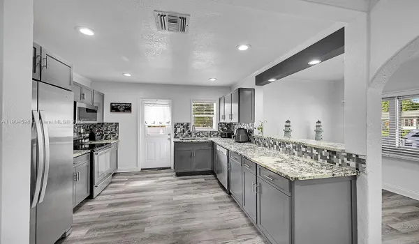 Arched Walkways, Baseboards Wall, Crown Molding, Drywall, Gray Cabinets, Kitchen Peninsula, Natural Light, Opens To Living Area, Pass Through Window, Recessed Lighting, Shaker Cabinets, Stone Countertops, Textured Ceiling, Textured Wall, U Shaped Kitchen, Vent, Wood Finish Floor, Arched Walkways, Drywall, Shaker Cabinets, Textured Ceiling, Vent