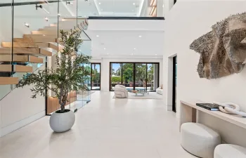 Dramatic two-story foyer with floating glass staircase, modern art accents, and direct views to the pool and waterfront beyond.