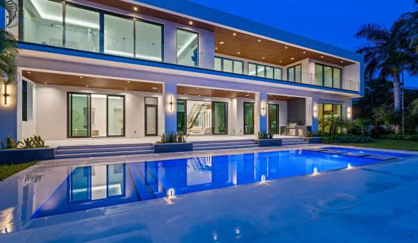 Stunning twilight view of the modern residence featuring glass-lined balconies, covered terraces, and a glowing pool centerpiece.