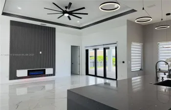 Living area with a tray ceiling, a glass covered fireplace, and ceiling fan