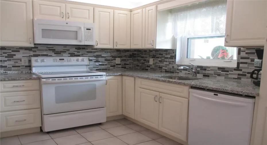 A BRIGHT KITCHEN WITH GRANITE COUNTERTOPS, CREAM COLORED CABINETS & WHITE APPLIANCES