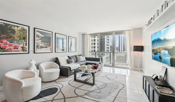 Modern open-concept living room with floor-to-ceiling windows offering panoramic views of Brickell skyline and Miami River. Luxury high-rise condo in the heart of Brickell.