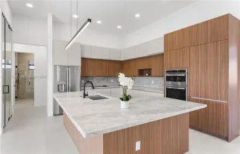 The CHEF'S KITCHEN offers OVERSIZED L-SHAPED ISLAND w/ MARBLE COUNTERTOP & extra entertainment space! Custom cabinetry, MARBLE TAJ MAHAL COUNTERTOPS w/ FULL BACKSPLASH, large pantry & premium GE appliances including wall oven, microwave, electric cooktop, dishwasher, refrigerator and freezer, plus a large sink with black fixtures.