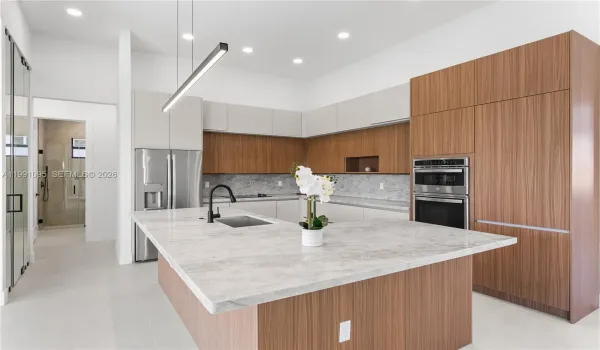 The CHEF'S KITCHEN offers OVERSIZED L-SHAPED ISLAND w/ MARBLE COUNTERTOP & extra entertainment space! Custom cabinetry, MARBLE TAJ MAHAL COUNTERTOPS w/ FULL BACKSPLASH, large pantry & premium GE appliances including wall oven, microwave, electric cooktop, dishwasher, refrigerator and freezer, plus a large sink with black fixtures.