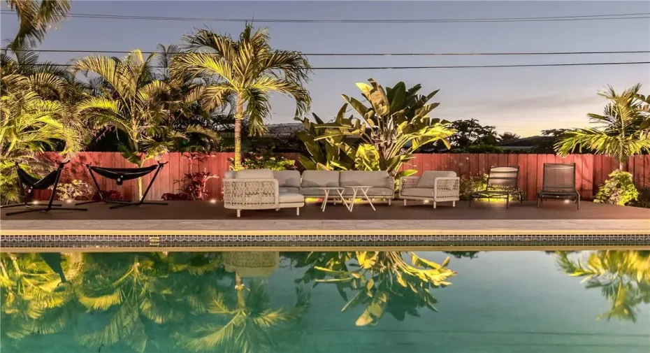 Tropical Fenced in Private Backyard with Heated Pool, uplighting, outdoor dining table, lounge chairs and plenty of seating/hammocks.