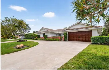 Front exterior of the home featuring a wide circular driveway, attached garage, mature landscaping, and well maintained lawn.