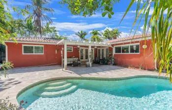 Rear elevation with covered patio, French doors, and multiple windows overlooking the pool. Tile roof and landscaped yard enhance the outdoor setting.