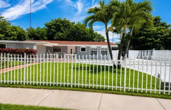 Front elevation featuring a fully fenced yard, mature palm trees, and ample parking.
