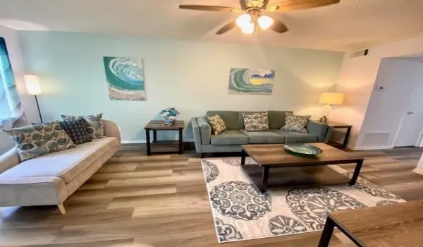 Open living area featuring wood-finish flooring, light blue wall paint, a ceiling fan with integrated lighting, and a white textured ceiling