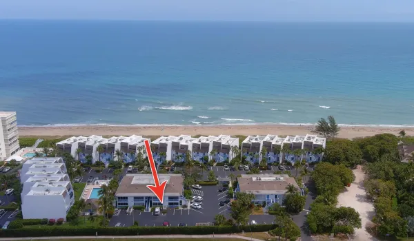 Drone shot highlighting a condo adjacent to the ocean, private beach access, and lush tropical landscaping.