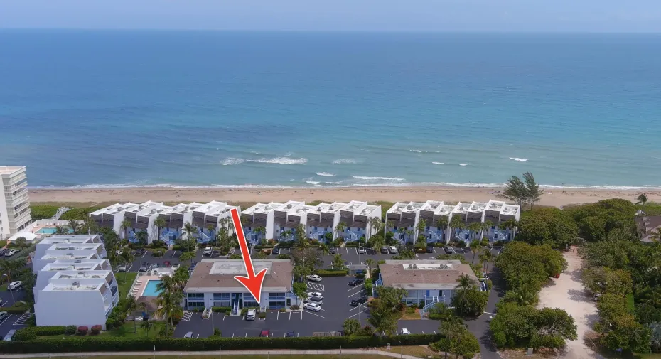 Drone shot highlighting a condo adjacent to the ocean, private beach access, and lush tropical landscaping.