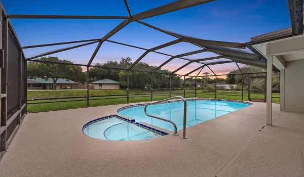 Screened enclosure featuring a freeform swimming pool with integrated spa, concrete deck, and perimeter fencing