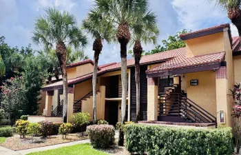 Multi-story building featuring a stucco exterior, red tile roofing, and prominent palm trees