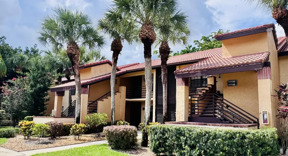 Multi-story building featuring a stucco exterior, red tile roofing, and prominent palm trees