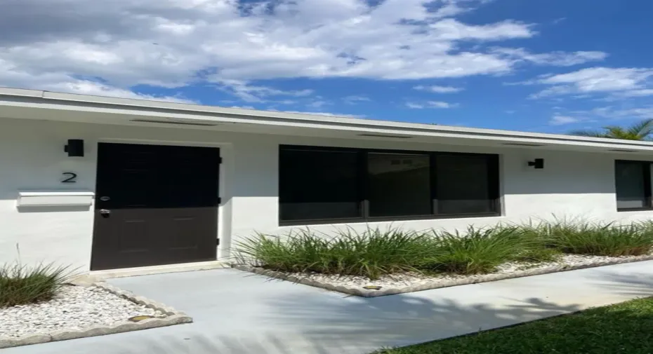 Contemporary white stucco exterior with dark entry door, modern black wall sconces, and dark-framed windows