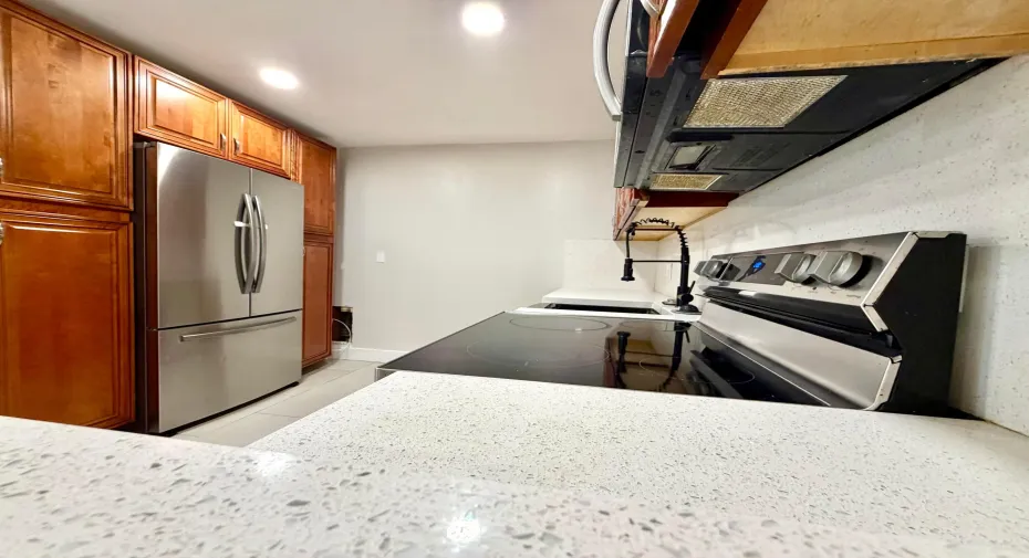 Contemporary kitchen featuring light-toned countertops, full-height backsplash, wood-finish cabinetry, stainless steel appliances, and a black gooseneck faucet
