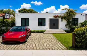 Beautifully renovated contemporary residence featuring a striking modern façade, elegant oversized entry, lush tropical landscaping, and a spacious two-car driveway with EV charging.