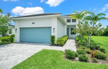 Contemporary exterior featuring a two-car garage with a blue door, a paver driveway, an inviting paver walkway, lush landscaping, and a well-manicured lawn