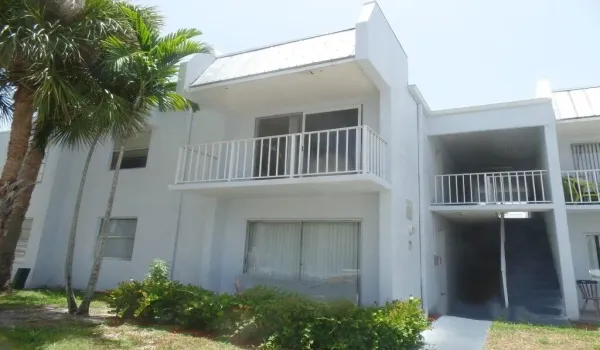 Multi-story stucco exterior featuring a second-floor balcony with white railings, sliding glass doors, and a metal roof