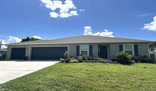 Contemporary stucco exterior featuring a three-car garage, a front entry, and a landscaped garden bed