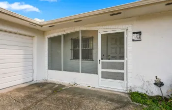 Covered and screened front entry with white brick detail, a protected walkway, and direct access to the home and two car garage. This practical entry space adds an extra layer of privacy and comfort while creating a welcoming transition into the home.