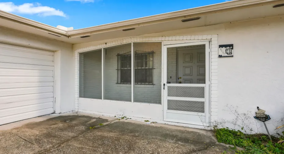 Covered and screened front entry with white brick detail, a protected walkway, and direct access to the home and two car garage. This practical entry space adds an extra layer of privacy and comfort while creating a welcoming transition into the home.