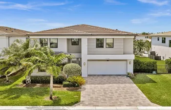 Two-story contemporary residence featuring a tiled roof, paver driveway, integrated garage, manicured landscaping, and exterior wall sconces