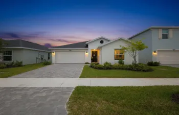 Contemporary single-story residence featuring a paver driveway, an attached garage, a covered entry, and established landscaping