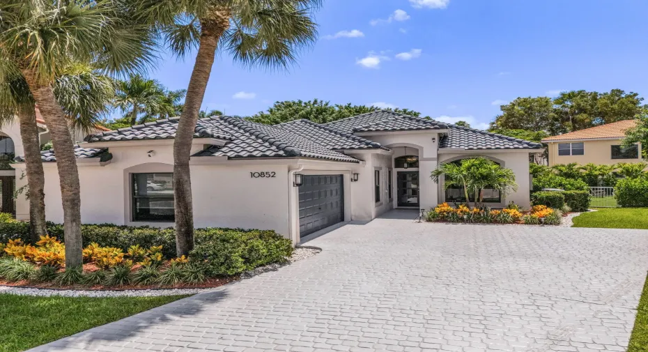 Contemporary stucco residence featuring a dark tile roof, a paver driveway, and an arched entry