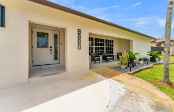 Welcoming front entry featuring a double door with decorative glass inserts, covered patio space, and manicured landscaping with gravel accents