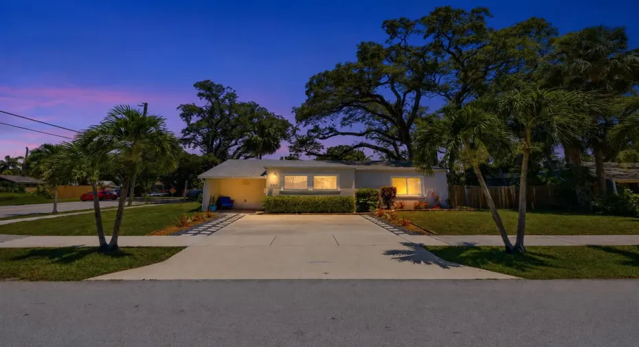Single-story residence featuring a paved driveway, manicured lawn, and mature palm trees