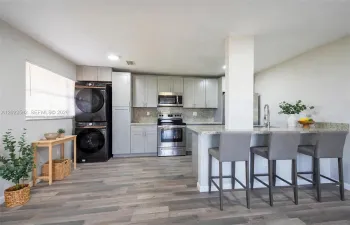 Kitchen featuring grey cabinetry, stone-finish countertops, stainless steel appliances, built-in laundry station, and wood-finish flooring