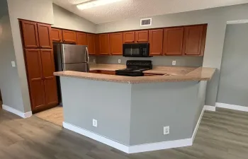 Kitchen featuring wood-finish cabinetry, stainless steel refrigerator, black microwave, and black electric range