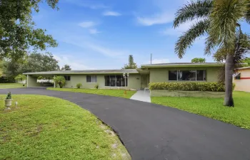 Ranch-style exterior with a pale green stucco finish, a covered carport, and a paved driveway
