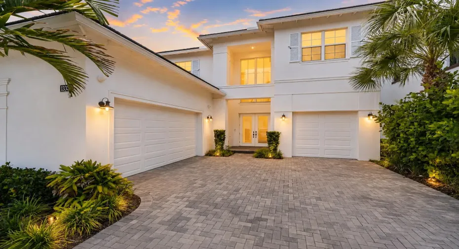 Two-story home exterior with three-car garage and paver driveway at dusk