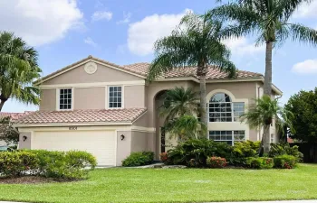 Stucco exterior with a tiled roof, featuring an arched window, multiple palm trees, a well-maintained lawn, and established landscaping