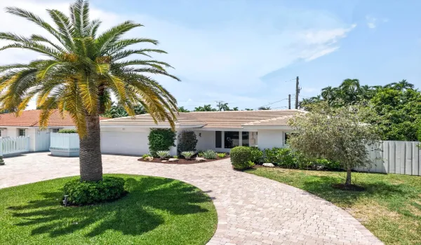 Exterior residence featuring a paver driveway, mature palm tree, lush landscaping, white stucco facade, and a tile roof