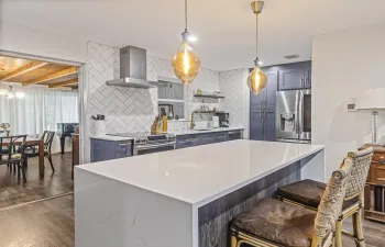 Modern kitchen w quartz waterfall-edge island and stainless steel appliances.