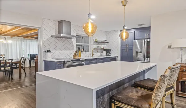 Modern kitchen w quartz waterfall-edge island and stainless steel appliances.