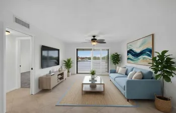 Spacious living area featuring neutral tile flooring, white walls, a ceiling fan, and sliding glass doors with white louvered shutters opening to a scenic water backdrop