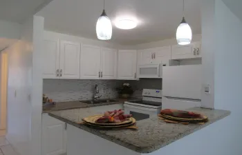 Kitchen featuring white cabinetry, light-toned granite countertops, a mosaic tile backsplash, and stainless steel sink