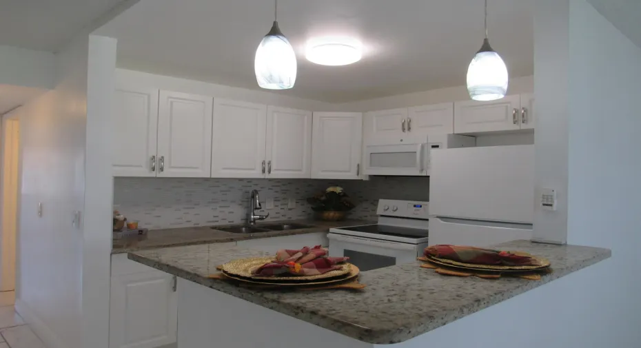 Kitchen featuring white cabinetry, light-toned granite countertops, a mosaic tile backsplash, and stainless steel sink