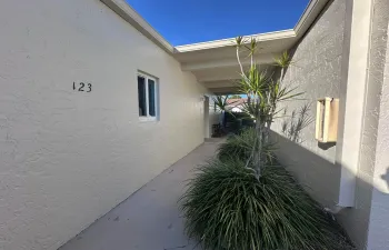 Covered walkway entrance featuring stucco exterior, a single window, and integrated planter beds with mature tropical foliage
