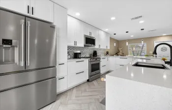 Modern kitchen featuring white cabinetry, stainless steel appliances, herringbone wood-finish flooring, a patterned tile backsplash, and a large island with an undermount sink