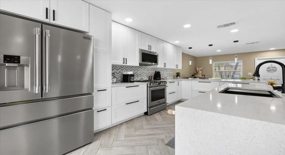 Modern kitchen featuring white cabinetry, stainless steel appliances, herringbone wood-finish flooring, a patterned tile backsplash, and a large island with an undermount sink