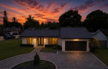 Contemporary exterior featuring a dark standing seam metal roof, white painted brick facade, a two-car garage, and a paver driveway